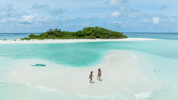 A beach with clear turquoise water, a small island with dense vegetation, and two people walking on the sand. - Stay Mikado (Thimarafushi)