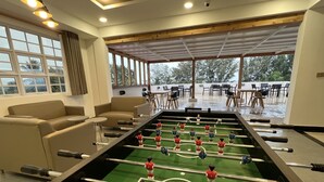 A foosball table in a room with large windows, a sofa, and a view of an outdoor patio area. - Stay Mikado (Thimarafushi)