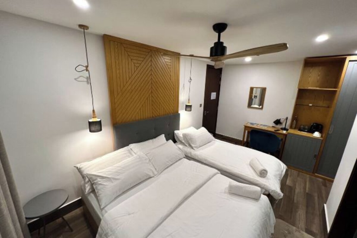 A hotel room with a large bed, a desk, a chair, a wardrobe, and a ceiling fan.
