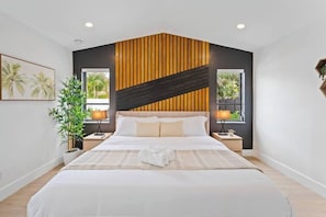 A modern hotel room with a large bed, two bedside tables, a potted plant, and a window with a view.
