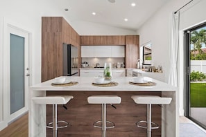 A modern kitchen with a central island, bar stools, and a view of the outdoors.