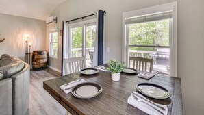 Zona pranzo con tavolo in legno apparecchiato per quattro persone, un divano in pelle e vista all'aperto attraverso ampie finestre.