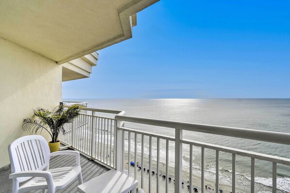 Un balcon donnant sur la plage, avec des chaises blanches et un pot de fleurs.