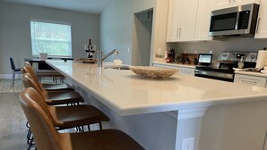 Una cocina moderna con una isla grande, taburetes de bar y un microondas.