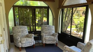 A sunroom with two ocean-themed armchairs, a blue rug, and a small table with a bottle.