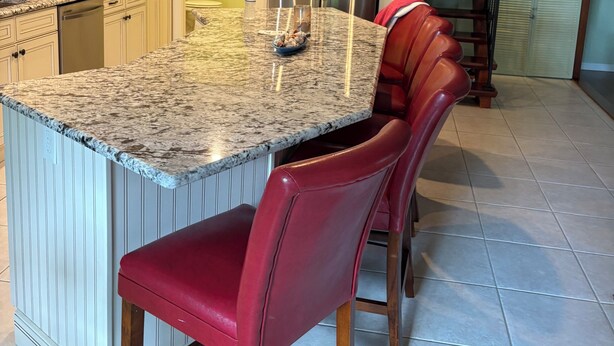 A kitchen with a granite island, red bar stools, and a stainless steel refrigerator.