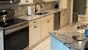A modern kitchen with stainless steel appliances, beige cabinetry, and a granite countertop.