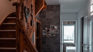 Een houten trap leidt naar een slaapkamer met een stenen muur en een raam.