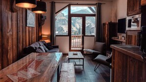 Een gezellige kamer met houten wanden, een groot raam met uitzicht op de bergen, een houten tafel, een bank en een klein tafeltje.