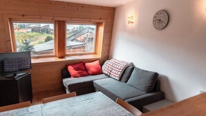 A cozy room with a wooden ceiling, a sofa with red and patterned cushions, a television on a stand, and a table with a patterned tablecloth. - Immodreams - La Patinoire - Avoriaz (Avoriaz)