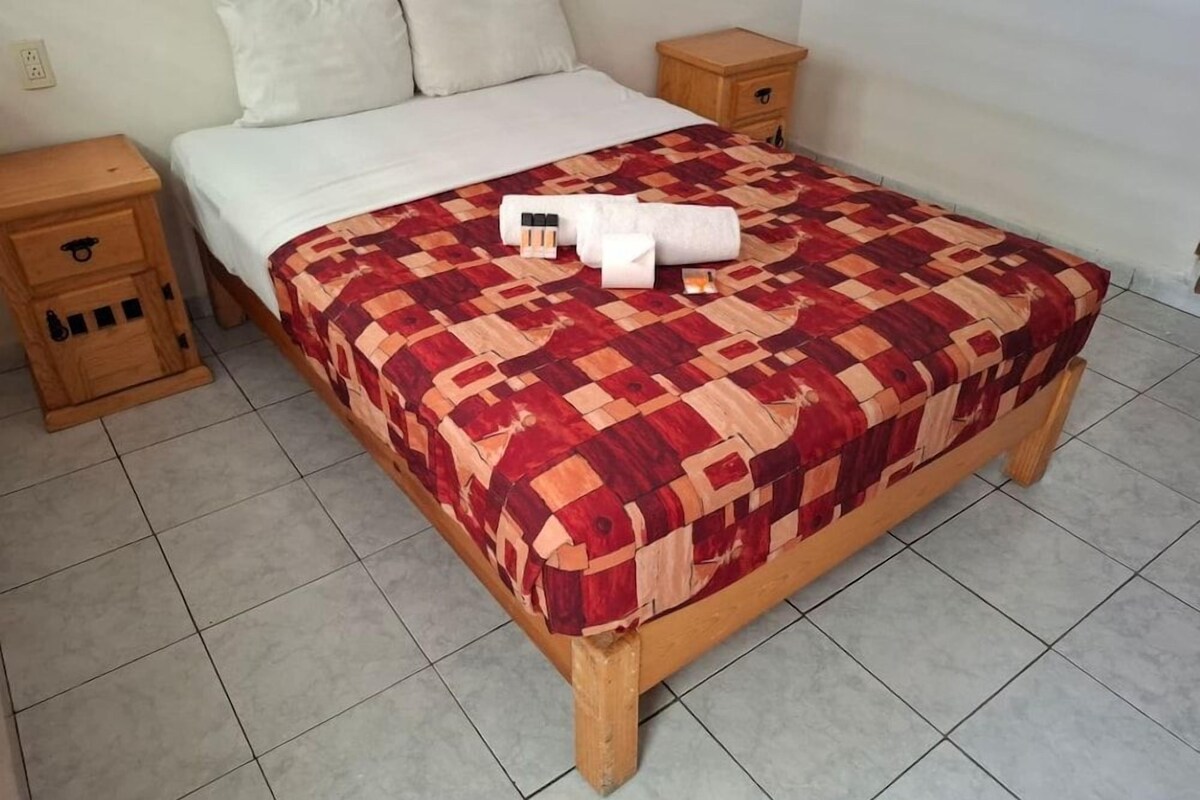 A single bed with a patterned bedspread, two bedside tables, and a wooden nightstand.
