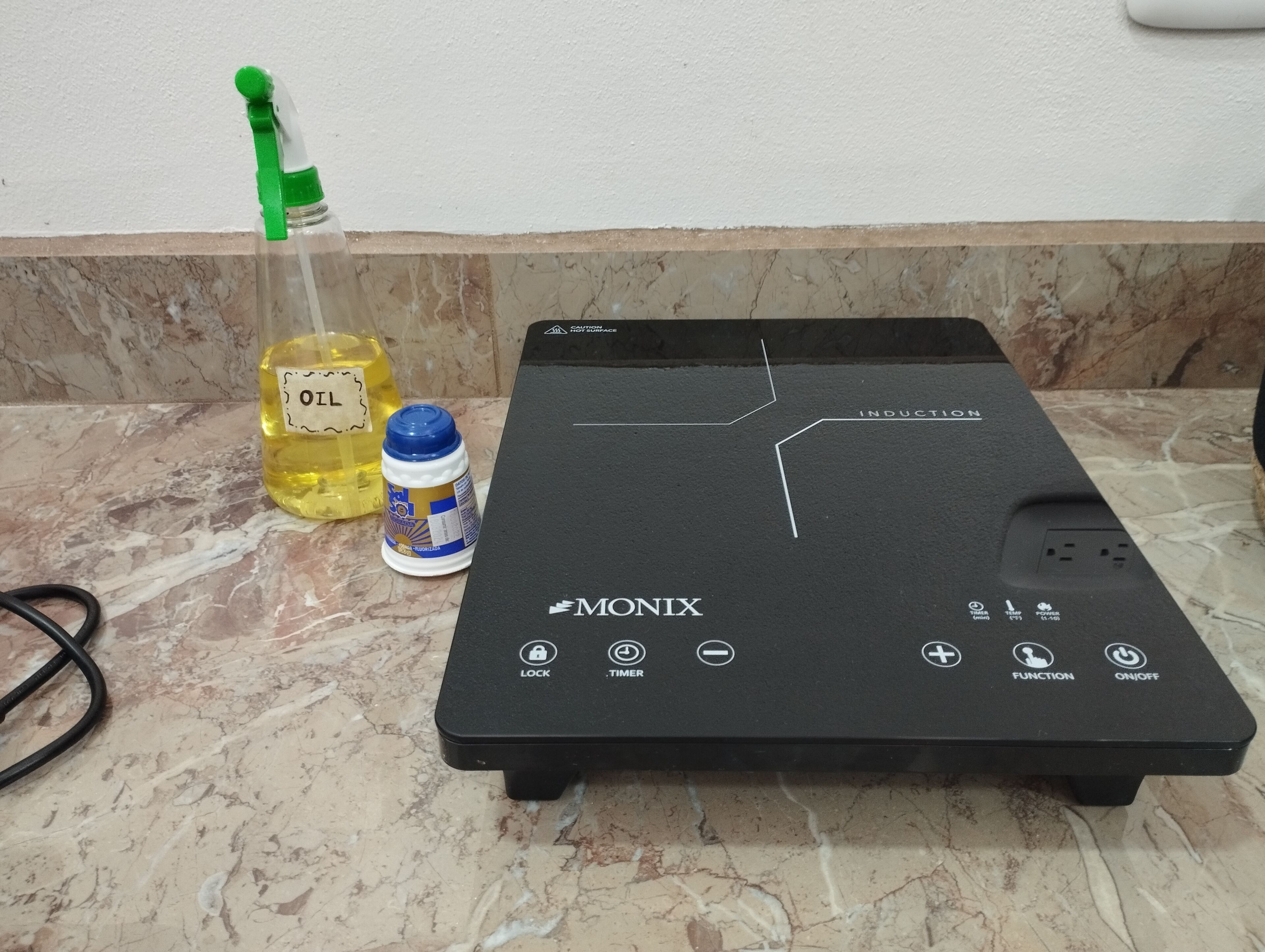 A black induction cooktop with a control panel, a bottle of oil, and a bottle of dish soap on a marble countertop.