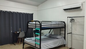 Een slaapkamer met een stapelbed, bureau, stoel en airconditioning.