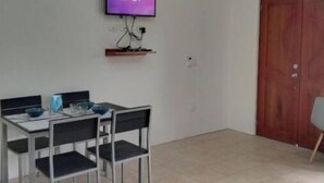 Een eethoek met een tafel en stoelen, een aan de muur bevestigde televisie, en een houten deur.