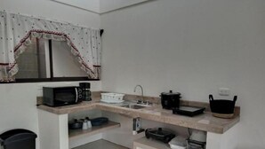 Een kleine keuken met een magnetron, koffiezetapparaat, spoelbak en opbergplanken.