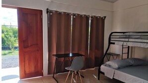 Een studentenkamer met een stapelbed, een bureau, een stoel en een gordijn.