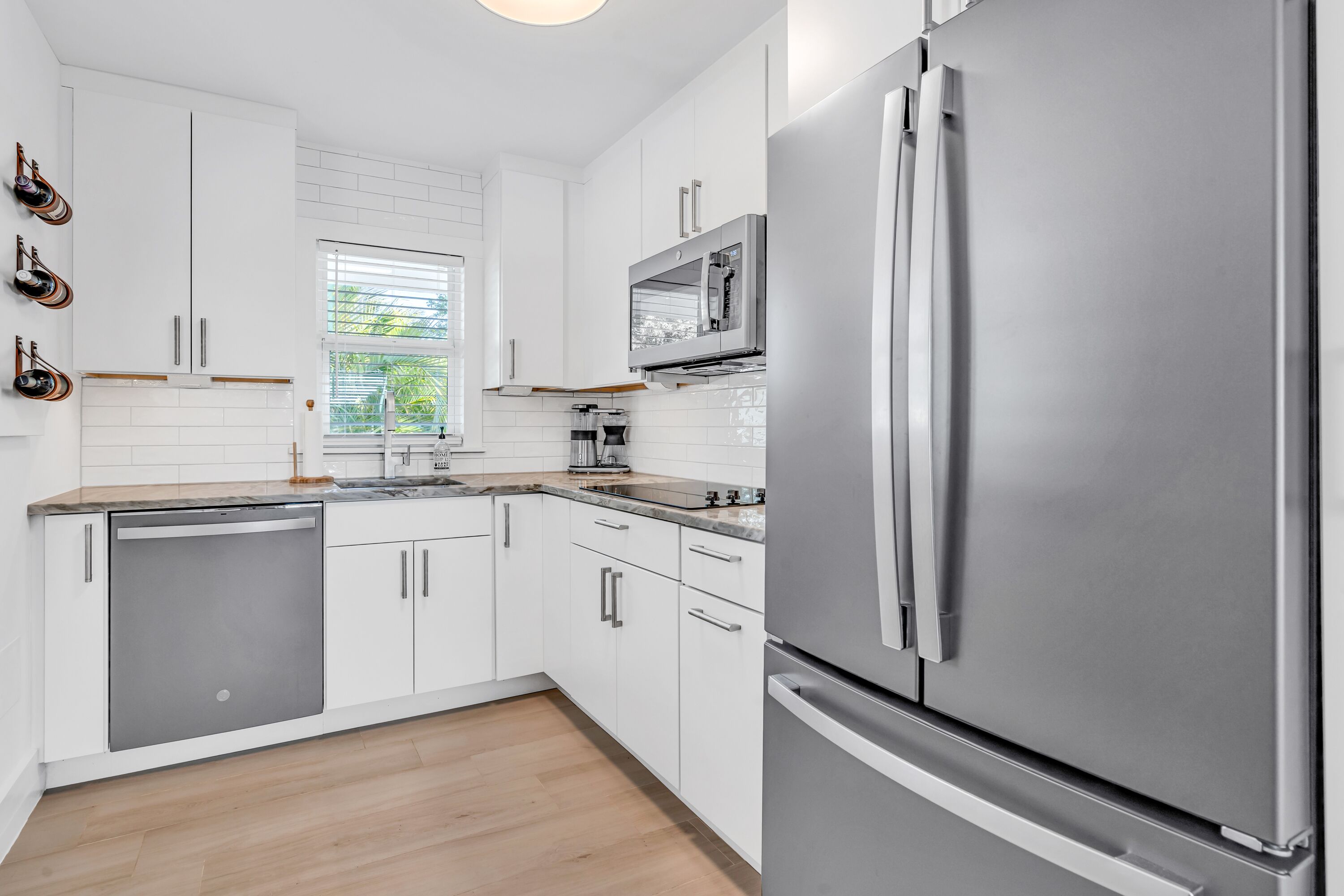A modern kitchen with white cabinetry, stainless steel appliances, and a window with blinds.