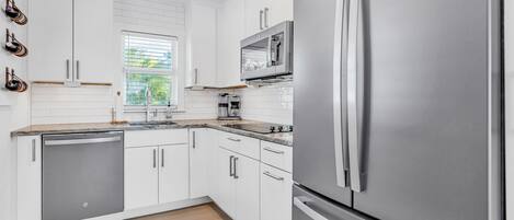 A modern kitchen with white cabinetry, stainless steel appliances, and a window with blinds.