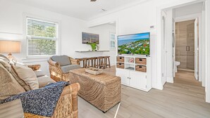 Un salon spacieux doté d’un grand téléviseur, de meubles en osier et offrant une vue sur l’extérieur grâce aux fenêtres.