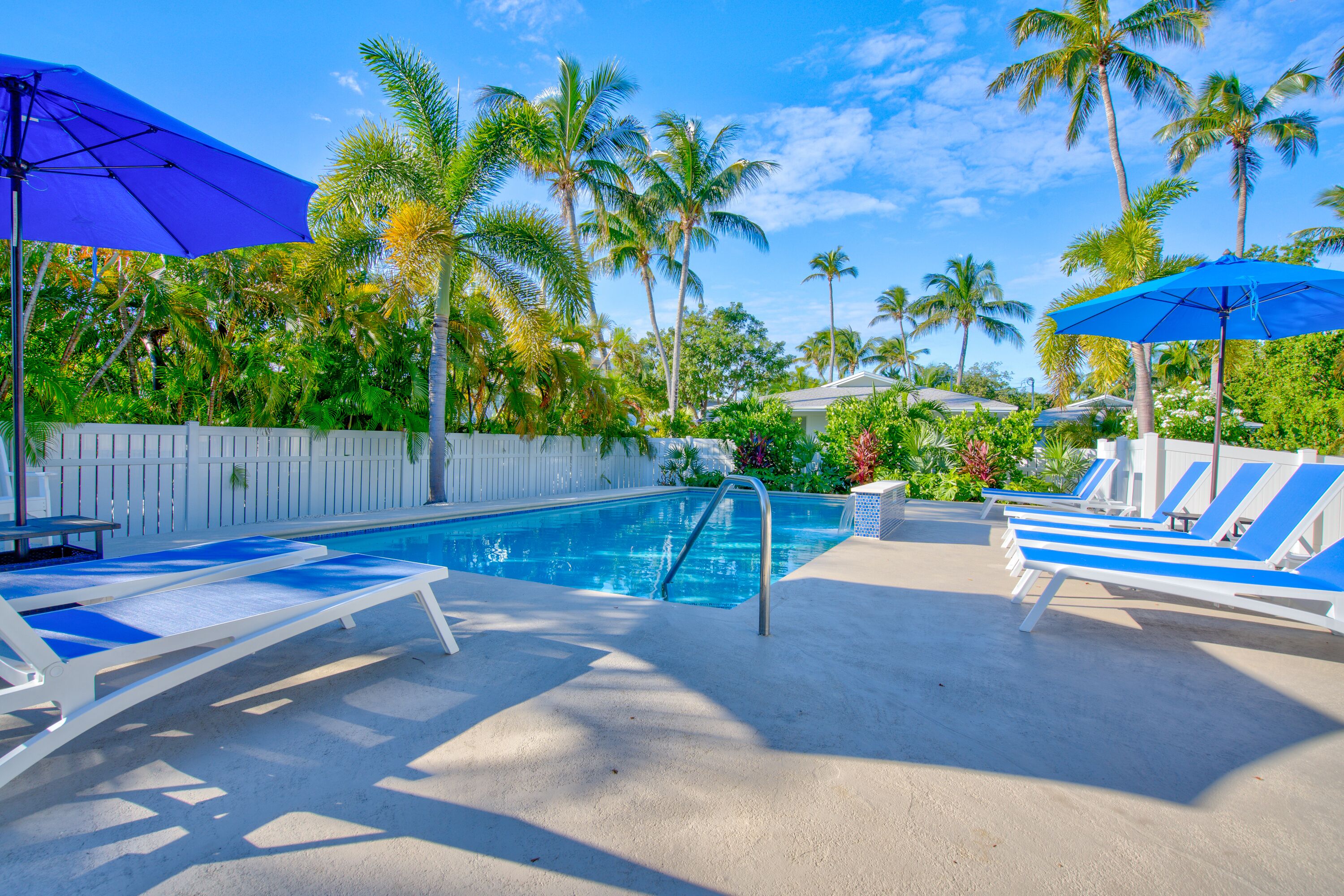 A pool area with lounge chairs, umbrellas, and palm trees.