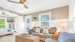 Un salon spacieux avec un grand canapé, une table basse et un téléviseur. Deux portes donnent accès à d’autres pièces, et les murs sont décorés d’étoiles de mer et d’un tableau.
