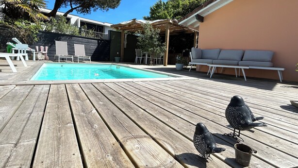 A wooden deck with a swimming pool, outdoor furniture, and decorative birds. - Chambre LES Pins (Mimizan)
