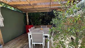 A wooden deck with a table and chairs, surrounded by greenery and a wooden fence. - Chambre LES Pins (Mimizan)