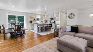 Una cocina moderna con armarios blancos, una isla central con taburetes y una zona de comedor con sillas de madera y una mesa.