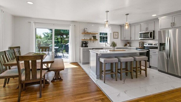 Una cocina moderna con una isla central, electrodomésticos de acero inoxidable y un comedor con mobiliario de madera.