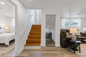 Amplia sala de estar con escalera de madera, un conjunto de sofás y una cama.