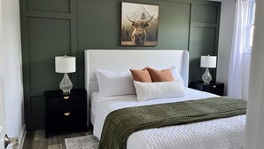 Un dormitorio con una cama, dos mesitas de noche y una pintura en una pared verde.