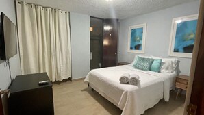 Un dormitorio con cama, escritorio, televisor y obras de arte en las paredes.