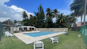 Una piscina con sillas de descanso, césped y palmeras.