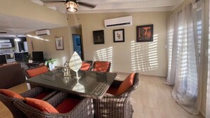 Un comedor con muebles de mimbre, una mesa de vidrio, ventilador de techo y unidades de aire acondicionado.
