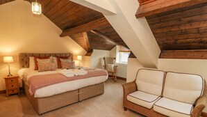 A bedroom with a large bed, a wicker sofa, and a wooden ceiling. - No. 2 The Mews (Carnforth)