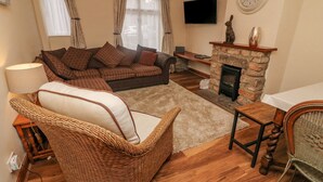 A cozy living room with a sofa, a wicker chair, a fireplace, and a television on the wall. - No. 2 The Mews (Carnforth)