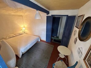 A bedroom with a bed, a small table, a lamp, and a door leading to another room.
