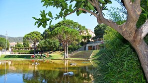 A serene park with a pond, trees, and a staircase leading to a building. - Costa Maresme, Barcelona, Clark´s 3 Bedroom TownHouse (Vilassar de Dalt)