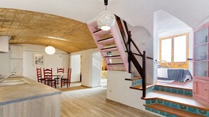 A spacious room with a wooden ceiling, a staircase with pink railings, a kitchen area with a sink and chairs, and a view of a bed through an open door. - Costa Maresme, Barcelona, Clark´s 3 Bedroom TownHouse (Vilassar de Dalt)