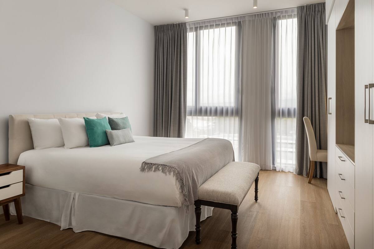 A modern bedroom with a large bed, a bench, a nightstand, and a wardrobe.