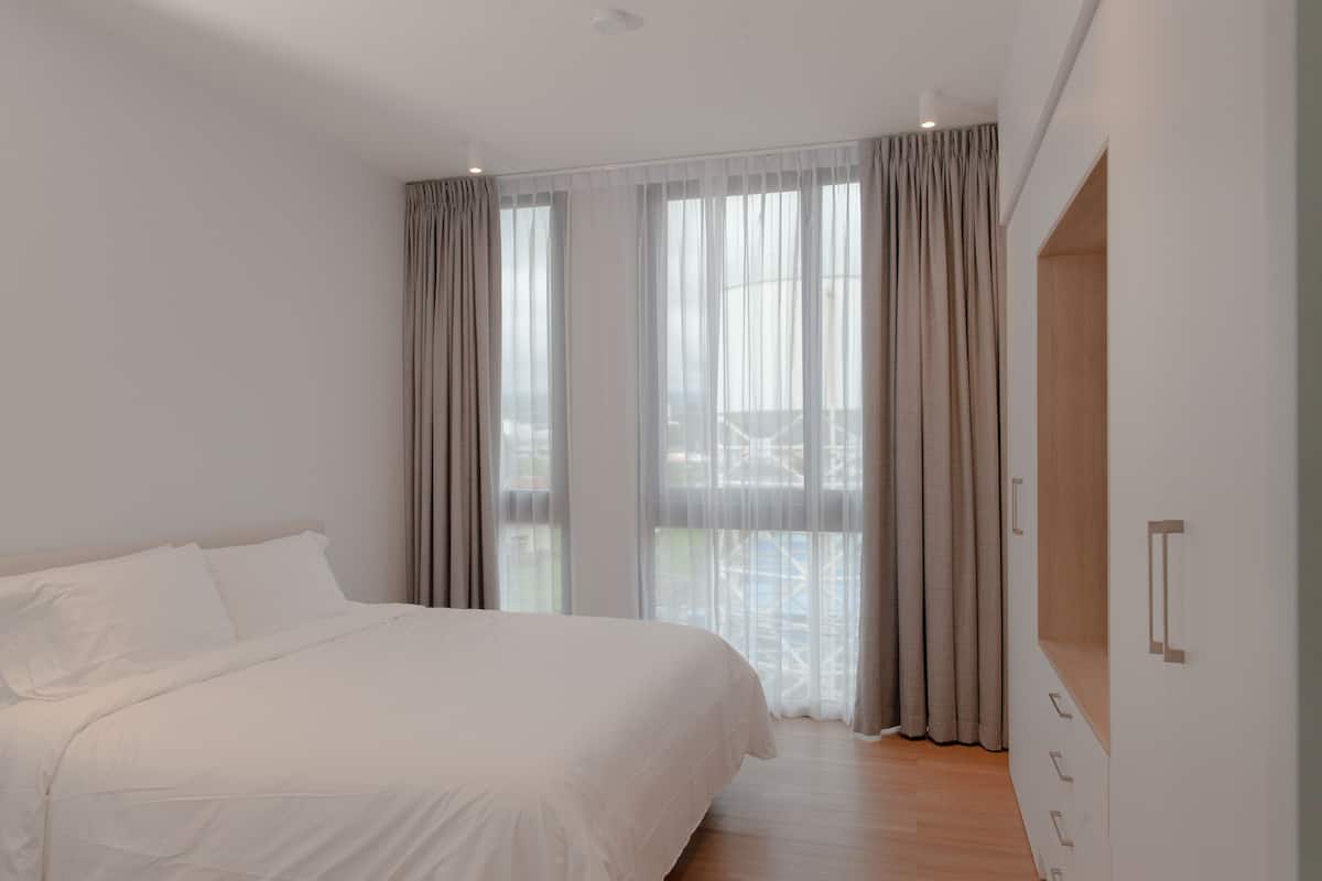 A modern bedroom with a large bed, a wardrobe, and a view of a balcony.