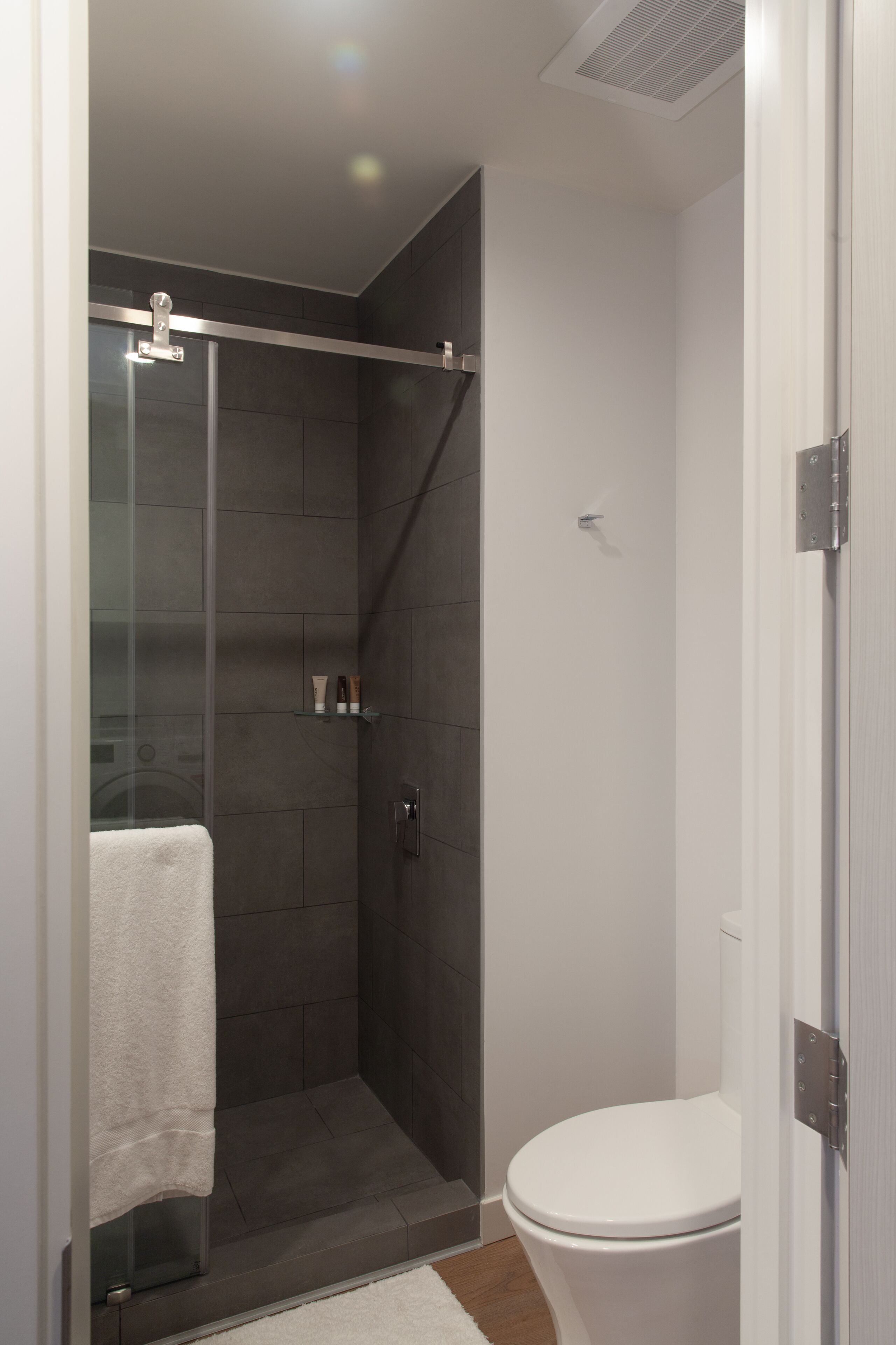 Een moderne badkamer met een douchecabine van glas, een wit toilet en een witte wastafel.