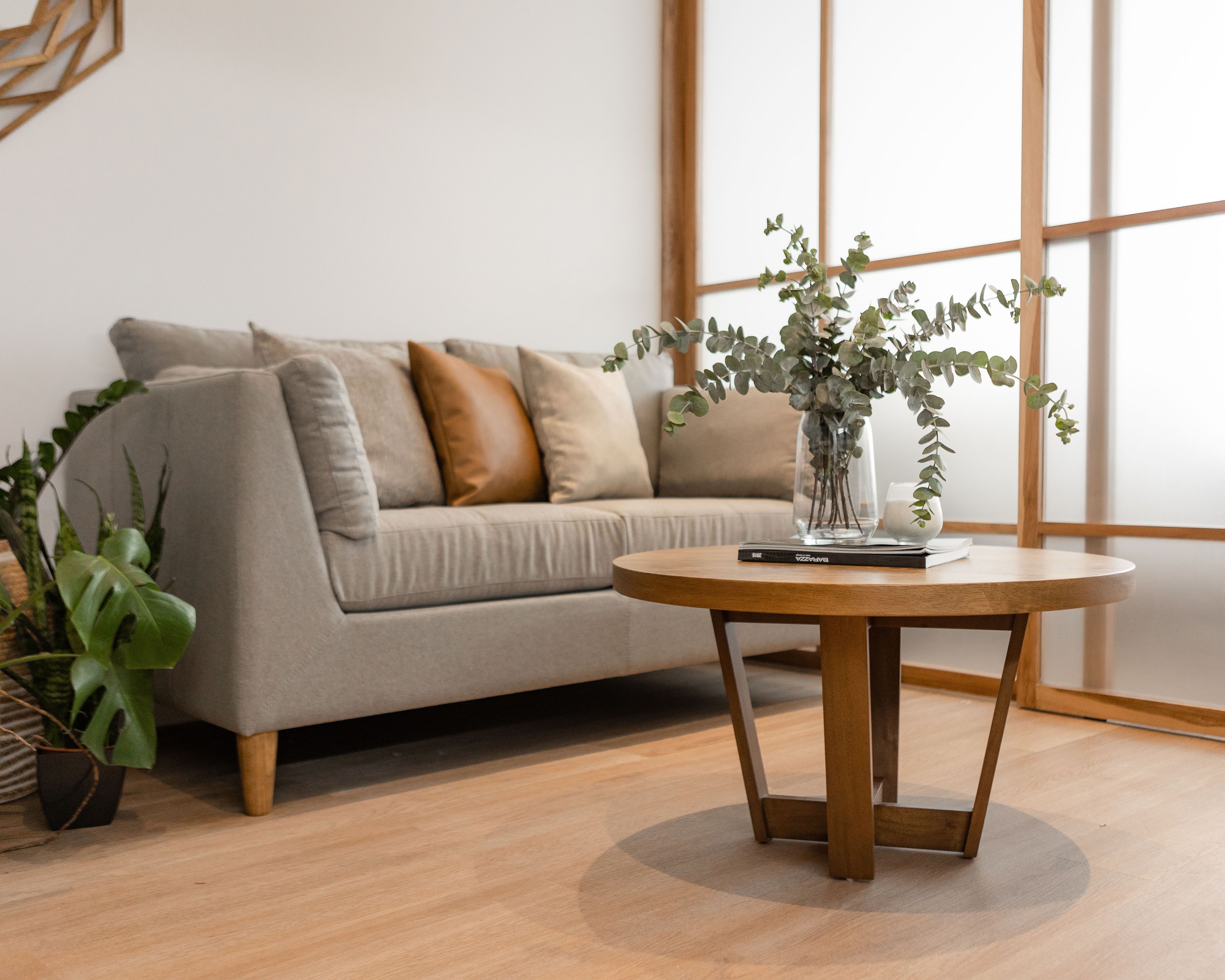 A modern living room with a grey sofa, a wooden coffee table, and a vase with green plants.