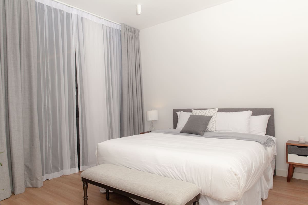 A bedroom with a bed, bedside table, lamp, and bench.