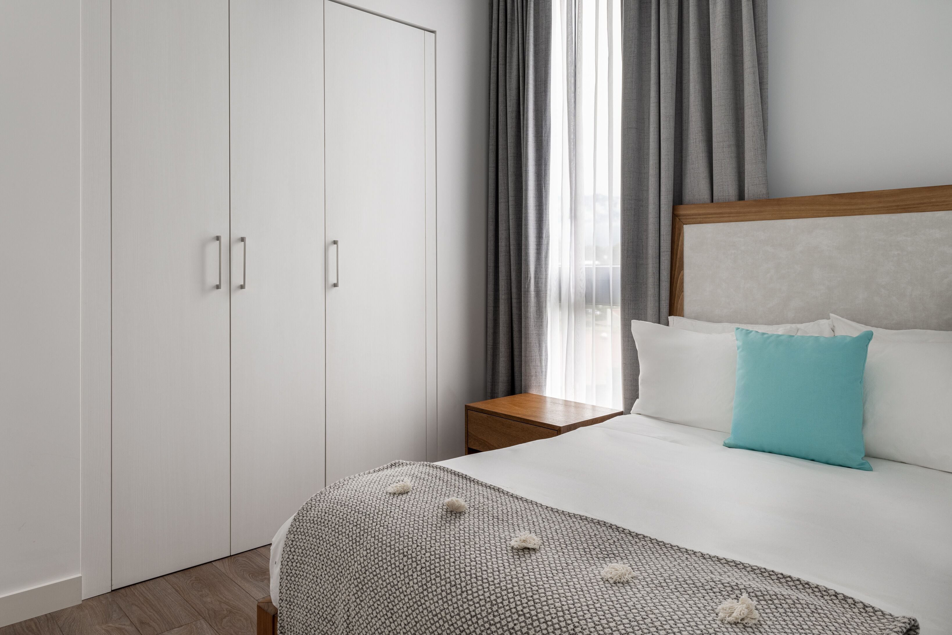 Un dormitorio con una cama, una mesita de noche, un armario y una ventana con cortinas.