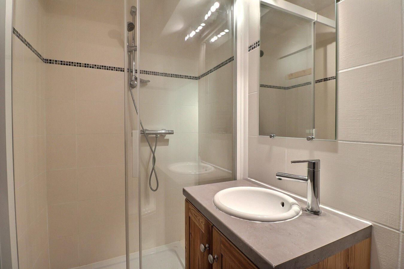 Une salle de bain moderne avec une douche à parois de verre, un lavabo blanc et un grand miroir au-dessus du meuble-lavabo.