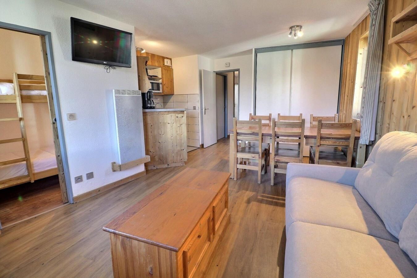 A compact living space with a sofa, wooden dining table, and a TV mounted on the wall.