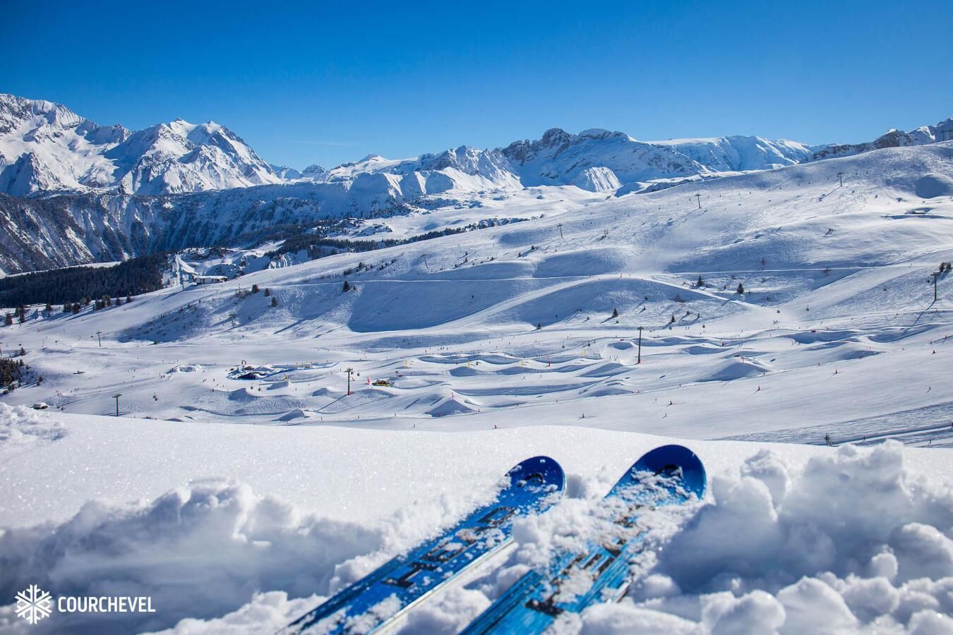 A snow-covered ski slope with a clear blue sky and mountains in the background.
