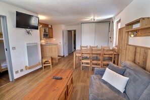 A living room with a wooden coffee table, a gray sofa, and a TV mounted on the wall. - 150m from resort center, 2nd floor, balcony, ski locker, 41m², La Tania (Courchevel)