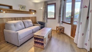 Un salon chaleureux avec un canapé, une petite table en bois et une vue sur les montagnes grâce à de grandes fenêtres.